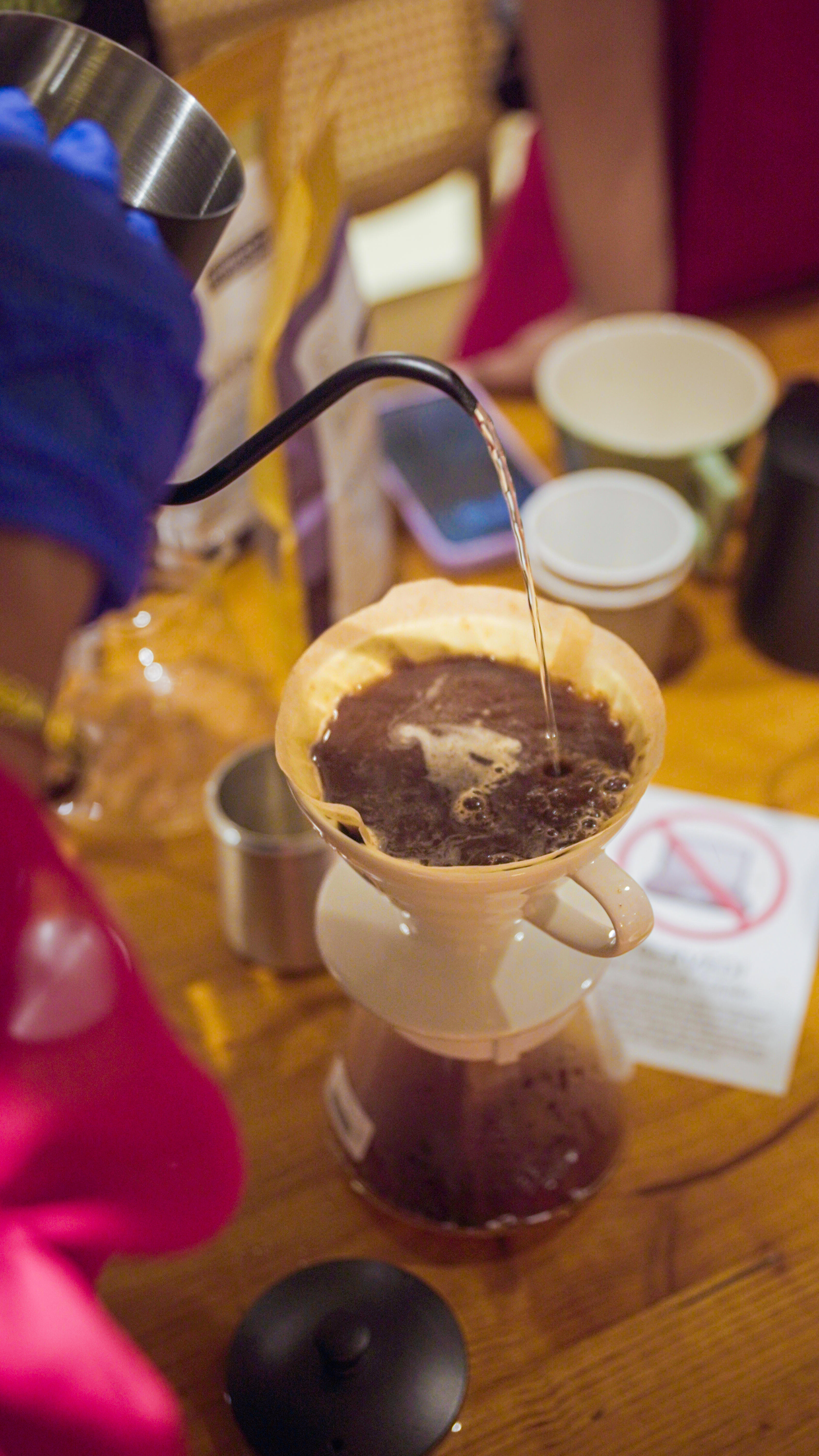 Pour over coffee brewing in progress with hot water filtering through coffee grounds into a cup below.